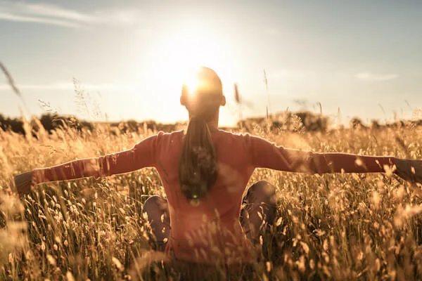 Woman sitting in a field of long grass at sunset