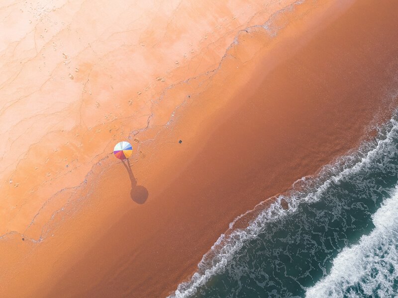 Aerial view of shoreline with sandy beach, an umbrella, and small waves