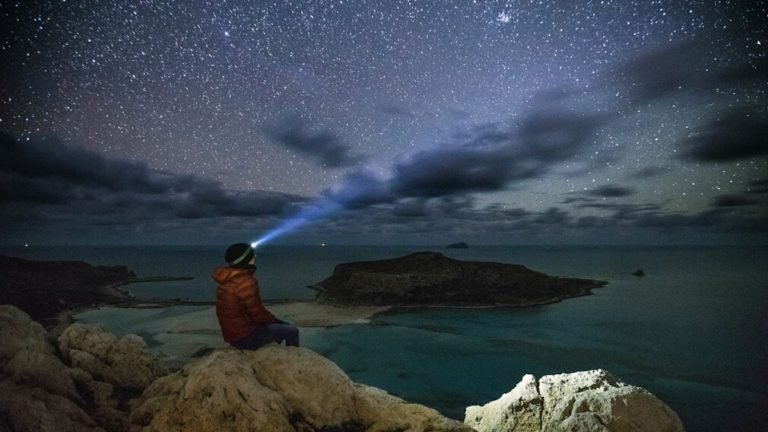 Person with headlamp watching starry night sky at a beautiful lagoon