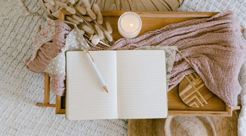 Blank journal with pen, scarf, and candle on bed table