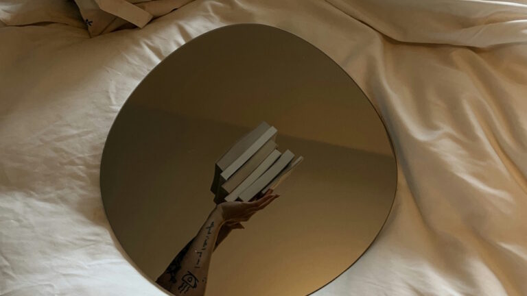 MIrror on bed showing reflection of hand holding books