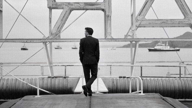 Man standing at a dock looking out at a harbour with ships