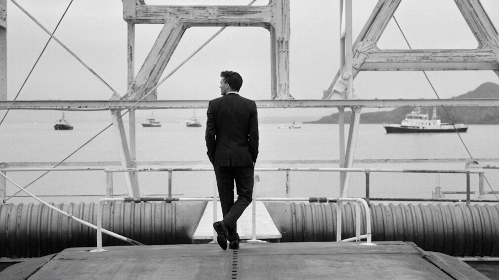 Man standing at a dock looking out at a harbour with ships