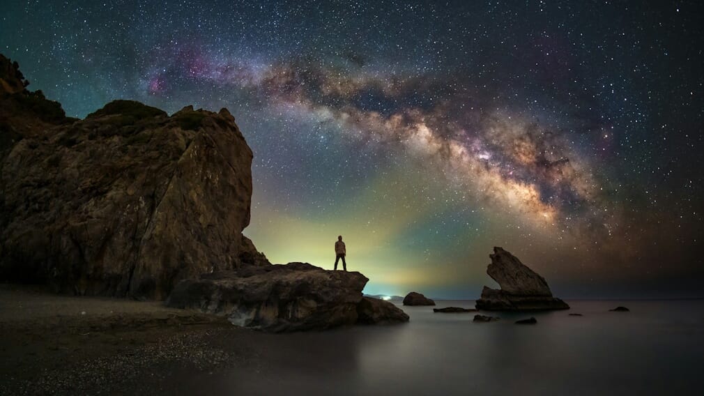 Man standing on rock looking up at a starry sky