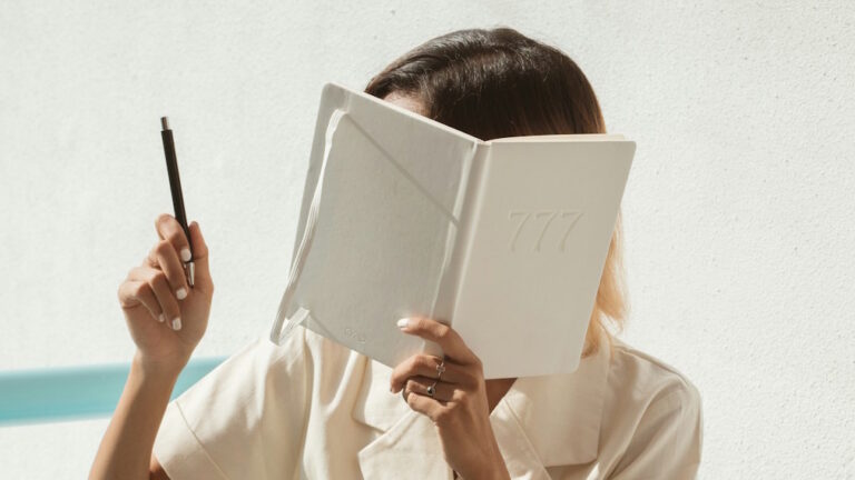 Woman holding pen and journal with 777 on the cover